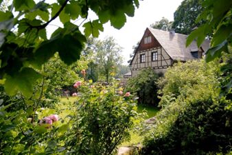 Der Landgasthof Haueis im traditionellen Fachwerkstil mit umgebenem gr&uuml;nen Garten und bl&uuml;henden Rosen in idyllischer Landschaft.