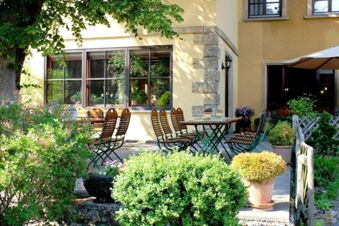 Sonnige Terrasse mit Holztischen und St&uuml;hlen umgeben von gr&uuml;nen Pflanzen im Landgasthof Haueis f&uuml;r entspannte Aufenthalte
