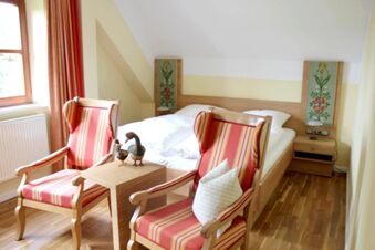 Helles, gem&uuml;tliches Schlafzimmer im Landgasthof Haueis mit zwei gestreiften Sesseln, Doppelbett und Holzfu&szlig;boden zu sehen.