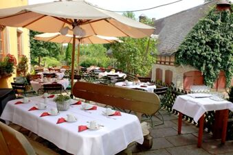 Terrasse des Landgasthof Haueis mit gedeckten Tischen, wei&szlig;en Tischdecken und Sonnenschirmen in idyllischer Gartenumgebung.