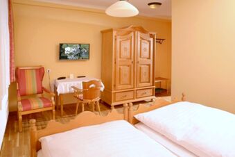 Helles gem&uuml;tliches Zimmer im Landgasthof Haueis mit zwei Einzelbetten, Holzm&ouml;beln und einem kleinen Tisch mit Stuhl und Sessel.