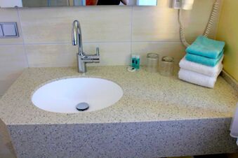 Heller Waschbeckenbereich mit moderner Armatur, gefalteten Handt&uuml;chern und Toilettenartikeln im Badezimmer des Landgasthof Haueis.