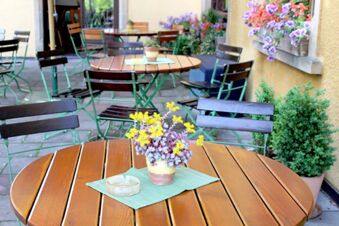 Gem&uuml;tlicher Au&szlig;enbereich mit Holztischen und gr&uuml;nen St&uuml;hlen sowie Blumenarrangements im Landgasthof Haueis.