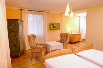 Gem&uuml;tliches G&auml;stezimmer im Landgasthof Haueis mit zwei Betten, antiken Sesseln, einem Tisch und dekorativem Schrank bei Tageslicht.