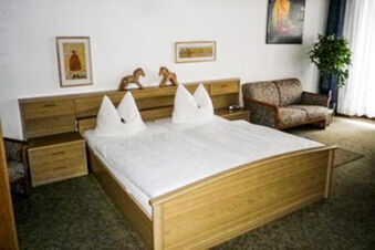 Helles G&auml;stezimmer im Landhotel-Restaurant Mei&szlig;nerhof mit einem gro&szlig;en Doppelbett, Sofa und dekorativen Holzpferden am Kopfbrett.
