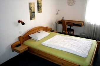 Ein einfach eingerichtetes Zimmer mit Holzbett, Schreibtisch und Fenster im Landhotel-Restaurant Mei&szlig;nerhof.