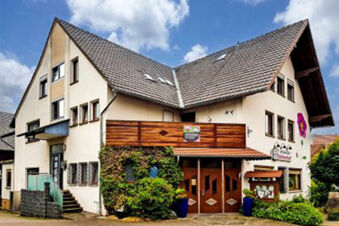 Fassade des Landhotel-Restaurant Mei&szlig;nerhof in einem traditionellen Geb&auml;ude mit Holzveranda, Pflanzen und blauen Himmel im Hintergrund.