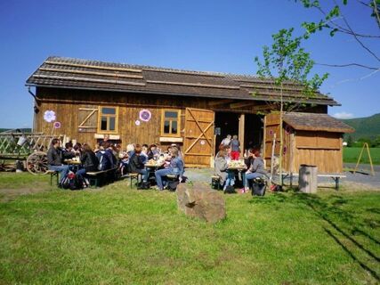 Gastgruppen sitzen an Tischen im Freien vor dem rustikalen Holzgeb&auml;ude vom Landhotel-Restaurant Mei&szlig;nerhof an einem sonnigen Tag.