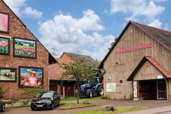 Au&szlig;enansicht des Landhotel-Restaurant Mei&szlig;nerhof mit dem Mohn-Kino und dekorativen Bildern an der Backsteinwand bei blauem Himmel.