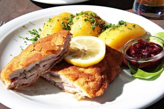 Ein Teller mit paniertem Schnitzel, Kartoffeln mit Petersilie, einer Zitronenscheibe und Preiselbeerso&szlig;e im Landhotel-Restaurant Mei&szlig;nerhof serviert.