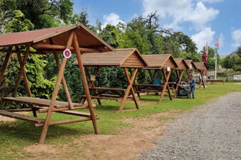 Reihen von &uuml;berdachten Holzb&auml;nken im Au&szlig;enbereich des Landhotel-Restaurant Mei&szlig;nerhof mit gr&uuml;ner Umgebung und Spazierweg.