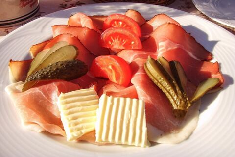 Ein Teller mit hauchd&uuml;nn geschnittenem Schinken, Gurkenscheiben, Tomaten und Butter im Landhotel-Restaurant Mei&szlig;nerhof sch&ouml;n angerichtet.