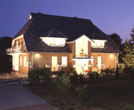 ライトアップされたランドハウス・ハイデ・ロマンチッチェス・ハイデホテル・ガルニ・ニヒトラウヒャーの夕暮れ時の眺め。手前には典型的なハーフティンバー様式の屋根と庭がある。