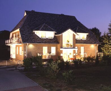 Skats uz izgaismoto Landhaus Heide Romantisches Heidehotel Garni Nichtraucher tumsā ar raksturīgo mūra jumtu un dārzu priek&scaron;plānā.
