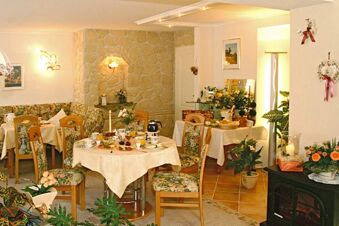 Dining area with floral chairs, round tables set for breakfast, plants, and stone wall at Landhaus Heide Romantisches Heidehotel Garni Nichtraucher