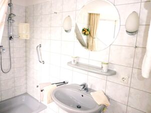 Bathroom with shower area, sink, round mirror, towel racks, and wall lights at Landhaus Heide Romantisches Heidehotel Garni Nichtraucher