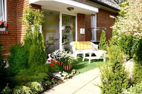Small garden patio with white bench and yellow cushions in front of a brick house at Landhaus Heide Romantisches Heidehotel Garni Nichtraucher