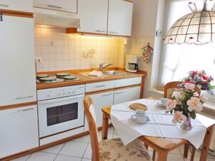 bright kitchen with white cabinets, stove, coffee maker, wooden table with flowers and cups at Landhaus Heide Romantisches Heidehotel Garni Nichtraucher