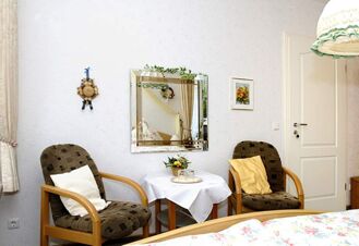 Two wooden armchairs with cushions flank a small table covered with white cloth in a room at Landhaus Heide Romantisches Heidehotel Garni Nichtraucher
