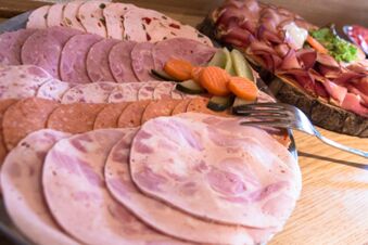 Verschiedene Wurst- und Schinkensorten mit eingelegtem Gem&uuml;se auf einem Holzbrett serviert im Hotel Gasthof Huber als Teil des Fr&uuml;hst&uuml;cksangebots.