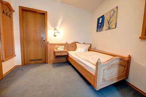 Cameră single confortabilă cu mobilier din lemn, pat și noptieră &icirc;n hotelul Gasthof Huber, mobilată &icirc;n stil tradițional.