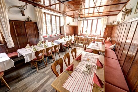 Gem&uuml;tlicher, traditionell eingerichteter Gastraum im Hotel Gasthof Huber mit Holzm&ouml;beln, roten Kissen und dekorierten Tischen an gro&szlig;en Fenstern.