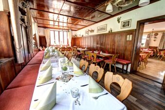 Im Restaurant des Hotel Gasthof Huber sind Tische mit wei&szlig;en und roten Tischdecken, auf denen gr&uuml;ne Servietten dekorativ gefaltet sind, einladend gedeckt.