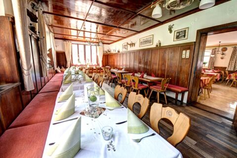 Im Restaurant des Hotel Gasthof Huber sind Tische mit wei&szlig;en und roten Tischdecken, auf denen gr&uuml;ne Servietten dekorativ gefaltet sind, einladend gedeckt.