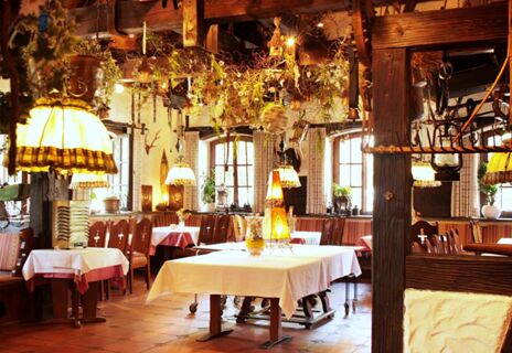 Rustikal dekorierter Speisesaal mit wei&szlig;en Tischdecken, Holzm&ouml;beln und warmem Licht im Hotel Lochm&uuml;hle GmbH.
