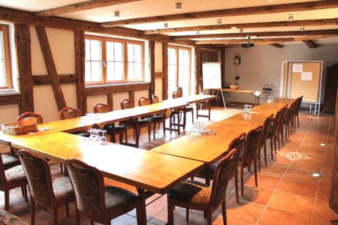 Ein heller und rustikaler Konferenzraum mit Holzvert&auml;felung und gro&szlig;en Fenstern im Hotel Lochm&uuml;hle GmbH, ausgestattet mit Tischen und St&uuml;hlen.