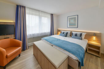 Modernes Hotelzimmer mit Doppelbett, blauem Bett&uuml;berwurf und orangem Sessel bei Meyenburg & Gerds H&ouml;ft Appartements am Wattenmeer