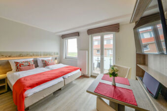 Helles und modernes Schlafzimmer mit zwei Einzelbetten, Tisch und Balkon im Meyenburg & Gerds H&ouml;ft Appartements am Wattenmeer.