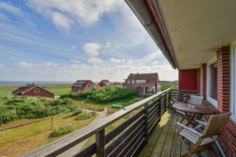 Balkon mit Holzm&ouml;beln und Blick auf gr&uuml;ne D&uuml;nenlandschaft und rote H&auml;user bei Meyenburg & Gerds H&ouml;ft Appartements am Wattenmeer