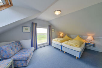 Hell eingerichtetes Schlafzimmer mit zwei Einzelbetten, gelber Bettw&auml;sche und Sofa im Meyenburg & Gerds H&ouml;ft Appartements am Wattenmeer.