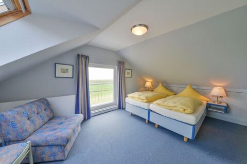 Hell eingerichtetes Schlafzimmer mit zwei Einzelbetten, gelber Bettw&auml;sche und Sofa im Meyenburg & Gerds H&ouml;ft Appartements am Wattenmeer.