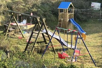 Spielplatz mit Rutschen, Schaukeln und Kletterger&uuml;sten auf einer Wiese bei Meyenburg & Gerds H&ouml;ft Appartements am Wattenmeer.