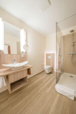 Modernes Badezimmer mit Dusche, Waschbecken und WC in hellen Holzt&ouml;nen bei Meyenburg & Gerds H&ouml;ft Appartements am Wattenmeer.