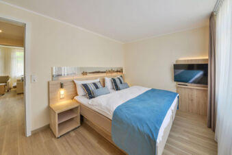 Modern eingerichtetes Schlafzimmer mit Doppelbett und Fernseher in den Meyenburg & Gerds H&ouml;ft Appartements am Wattenmeer.