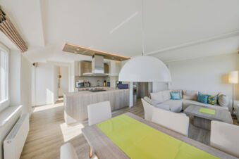 Modern eingerichtetes Wohn- und K&uuml;chenzimmer mit Sofa, Esstisch und Kochinsel bei Meyenburg & Gerds H&ouml;ft Appartements am Wattenmeer.