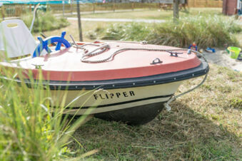 Kleines rotes und wei&szlig;es Boot namens Flipper auf einer Wiese mit Spielzeug im Hintergrund bei Meyenburg & Gerds H&ouml;ft Appartements am Wattenmeer