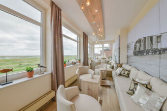 Heller und gem&uuml;tlicher Aufenthaltsraum mit gro&szlig;en Fenstern und Meerblick bei Meyenburg & Gerds H&ouml;ft Appartements am Wattenmeer.