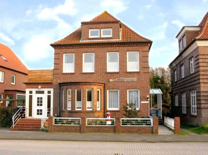 A brick two-story building with a tiled roof, white framed windows, a small garden with a fence, and a sign for Marinas Ferienwohnungen