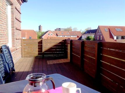 Balcony with wooden floor and railings overlooking rooftops and buildings under a clear sky at Marinas Ferienwohnungen