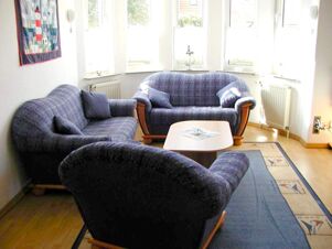 Living area with three blue patterned sofas, a small wooden coffee table, large windows, and a decorative rug at Marinas Ferienwohnungen