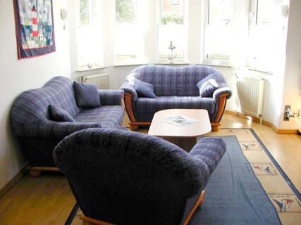 Living area with three blue patterned sofas, a small wooden coffee table, large windows, and a decorative rug at Marinas Ferienwohnungen