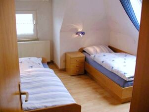 Two single beds with striped and floral bedding facing each other in a wooden floored room at Marinas Ferienwohnungen