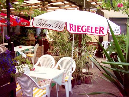 Au&szlig;enterrasse mit Tischen, St&uuml;hlen und Sonnenschirmen in einem gr&uuml;nen Bereich des Hotel-Restaurant zum Wilden Mann, gem&uuml;tlich und einladend.