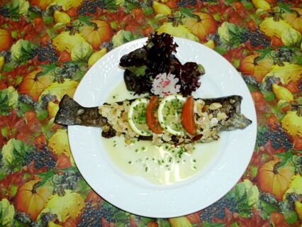 Gebratene Forelle mit Mandelbl&auml;ttchen, Zitronenscheiben, Tomate und Salat auf einem wei&szlig;en Teller im Hotel-Restaurant zum Wilden Mann serviert.