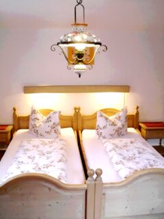 Zweibettzimmer mit Holzm&ouml;beln und floral gemusterten Bettdecken im Hotel-Restaurant zum Wilden Mann in gem&uuml;tlicher Atmosph&auml;re.