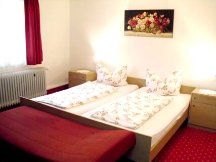 Gem&uuml;tlich eingerichtetes Zimmer mit zwei Einzelbetten, floralem Bettzeug und rotem Teppich im Hotel-Restaurant zum Wilden Mann.